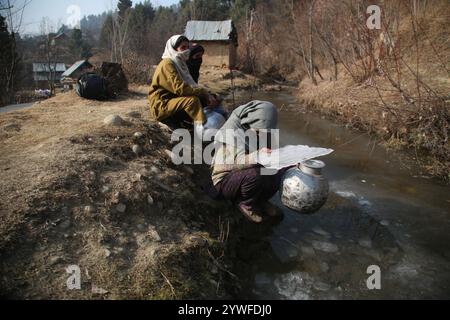 Srinagar, Indien. Dezember 2024. Die Frauen von Sonabanjran, einem abgelegenen Hügelland im Bezirk Pulwama in Südkaschmir, haben aufgrund der Temperaturen unter dem Gefrierpunkt große Schwierigkeiten. Da die Leitungswasserversorgung durch das Einfrieren der Versorgungsleitungen unterbrochen wurde, waren die Bewohner gezwungen, Trinkwasser aus einem gefrorenen Bach zu sammeln. (Foto: Nisar UL Haq Allaie/Pacific Press) Credit: Pacific Press Media Production Corp./Alamy Live News Stockfoto