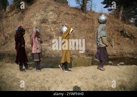 Srinagar, Jammu Und Kaschmir, Indien. Dezember 2024. Die Frauen von Sonabanjran, einem abgelegenen Hügelland im Bezirk Pulwama in Südkaschmir, haben aufgrund der Temperaturen unter dem Gefrierpunkt große Schwierigkeiten. Da die Leitungswasserversorgung durch das Einfrieren der Versorgungsleitungen unterbrochen wurde, waren die Bewohner gezwungen, Trinkwasser aus einem gefrorenen Bach zu sammeln. (Kreditbild: © Nisar UL Haq Allaie/Pacific Press via ZUMA Press Wire) NUR REDAKTIONELLE VERWENDUNG! Nicht für kommerzielle ZWECKE! Stockfoto