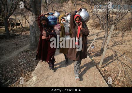 Srinagar, Jammu Und Kaschmir, Indien. Dezember 2024. Die Frauen von Sonabanjran, einem abgelegenen Hügelland im Bezirk Pulwama in Südkaschmir, haben aufgrund der Temperaturen unter dem Gefrierpunkt große Schwierigkeiten. Da die Leitungswasserversorgung durch das Einfrieren der Versorgungsleitungen unterbrochen wurde, waren die Bewohner gezwungen, Trinkwasser aus einem gefrorenen Bach zu sammeln. (Kreditbild: © Nisar UL Haq Allaie/Pacific Press via ZUMA Press Wire) NUR REDAKTIONELLE VERWENDUNG! Nicht für kommerzielle ZWECKE! Stockfoto