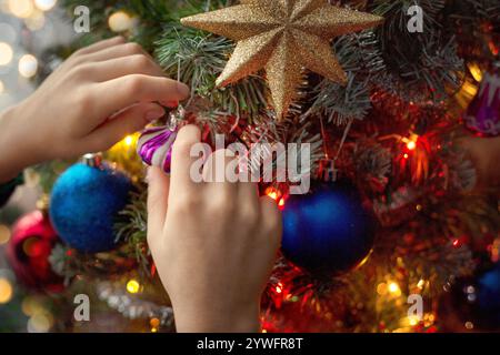 Kinderhände, die den Weihnachtsbaum in Nahaufnahme schmücken. Atmosphäre der Vorbereitung auf den Urlaub. Stockfoto