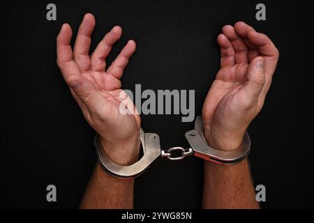 Mann mit Handschellen, der seine Handgelenke auf dunklem Hintergrund zeigt. Stockfoto