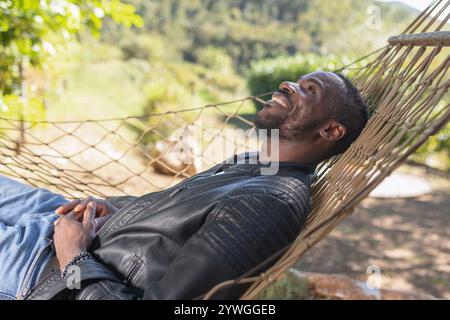 Unbeschwerter afroamerikanischer Mann, der einen Glamping-Kurzurlaub aus der Stadt genießt, während er sich in einer Hängematte entspannt. Stockfoto