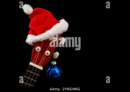 Weihnachtsmann roter Hut auf einem Gitarrenhals und eine blaue Kugel, isoliert auf Schwarz Stockfoto