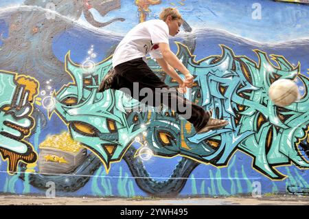 Ein zehnjähriger Junge spielt mit seinem Fußball vor einer Graffiti-Wand, Fußballplatz in Deutschland Stockfoto