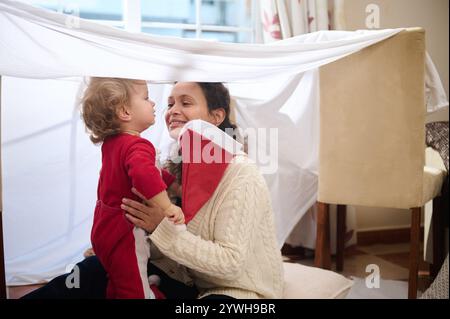 Ein freudiger Moment, in dem Mutter und Kind einen verspielten Moment in einer selbstgemachten Deckenfestung teilen. Stockfoto