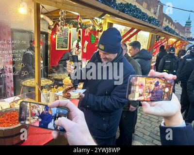 Warschau, Polen. Dezember 2024. Bayerns Ministerpräsident Markus Söder (CSU) genießt bei seinem Besuch in Warschau eine Würstchen auf einem Weihnachtsmarkt. Quelle: Marco Hadem/dpa/Alamy Live News Stockfoto