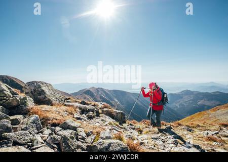 Backpacker-Frau in knallroter Jacke, die durch Bergketten mit Trekkingstöcken mit Hintergrund des Liptov-Tals geht, Westtatra, Slowakei. Aktive p Stockfoto