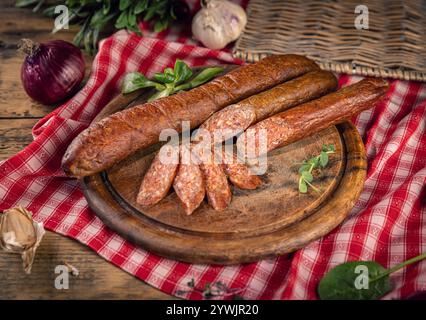 Wurst in Scheiben auf Holzbrett mit Kräutern und Gemüse auf rustikalem Tisch Stockfoto