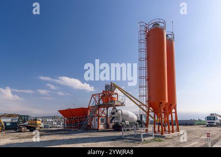 Betonmischanlage mit Mischturm und Zementwagen, die unter klarem Himmel geparkt sind Stockfoto