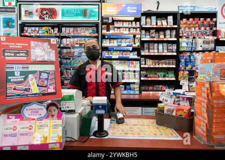 KUALA LUMPUR, MALAYSIA - 01. DEZEMBER 2023: Ein Kassierer posiert für ein Foto in einem 7-Eleven, einer globalen Lebensmittelhandelskette, die Snacks, Getränke und E anbietet Stockfoto