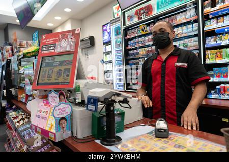 KUALA LUMPUR, MALAYSIA - 01. DEZEMBER 2023: Ein Kassierer posiert für ein Foto in einem 7-Eleven, einer globalen Lebensmittelhandelskette, die Snacks, Getränke und E anbietet Stockfoto