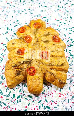 Nahaufnahme von weihnachtsbaum geformtem Rosmarin-Kräuter-Focaccia-Brot mit Kirschtomaten auf einem mehligen Backblech und stechpalme-Hintergrund Stockfoto