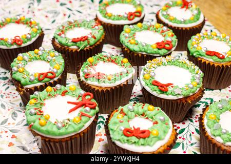weihnachts-Hackfleisch-Cupcakes bedeckt mit weißgoldener grüner und roter Zuckerglasur auf festlichem stechpalmen-Hintergrund Stockfoto