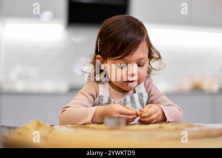 Niedliches kleines Mädchen, das Lebkuchenkekse mit einem Ausstecher in der Küche schneidet. Festliche Lebkuchen-Kekse Stockfoto