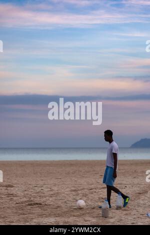 Junger Afroamerikaner mit einem Ball am Strand. Der Typ spielt Fußball am Sandstrand. Stockfoto