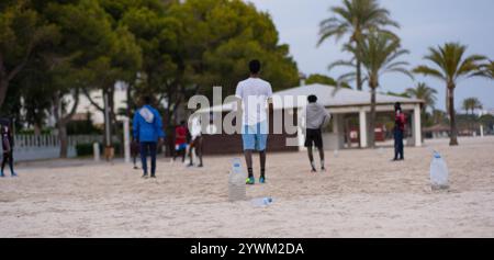 Junge Afroamerikaner spielen Fußball am Strand. Strandfußball mit improvisierten Fußballtoren aus Flaschen. Freizeit junger Männer Stockfoto
