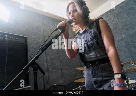 Weibliche Sängerin nimmt Gesang im professionellen Musikstudio auf. Frau in Kopfhörern, die in das Mikrofon zwischen Studiogeräten singt. Musikproduktion, Performance und Aufnahmekonzept. Stockfoto