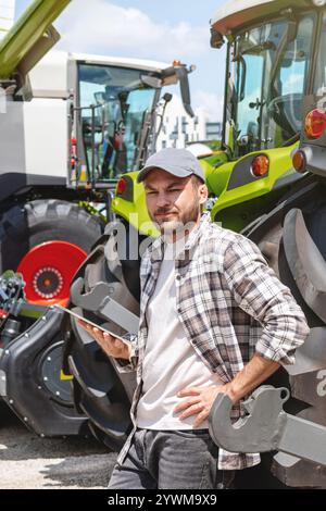 Landarbeiter mit digitalem Tablet gegen Traktor im Landmaschinenbetrieb. Stockfoto