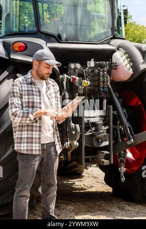 Landarbeiter mit digitalem Tablet gegen Traktor im Landmaschinenbetrieb. Stockfoto