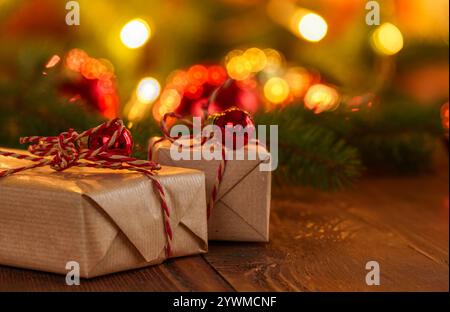 Nahaufnahme von zwei eingewickelten Weihnachtsgeschenken auf einem rustikalen Holztisch mit farbenfrohen Dekorationen und Lichtern im Hintergrund Stockfoto