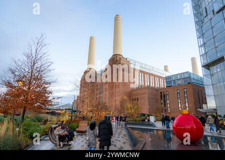 Menschen schlendern auf einem Fußweg, gesäumt von Chistmas Ligthen und Riesenkugeln im Battersea Power Station Stockfoto