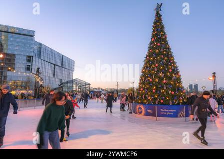 Bei Sonnenuntergang läuft man auf einer Eislaufbahn am Battesea Power Station um einen hohen Weihnachtsbaum Stockfoto