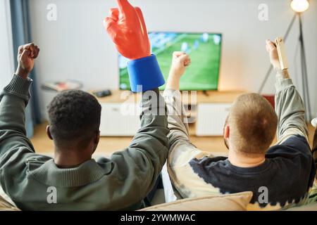 Rückansicht von begeisterten Sportfans, die Fußballspiele zu Hause im Fernsehen sehen, auf der Couch sitzen und die Hände heben, um den Sieg zu feiern, Kopierraum Stockfoto