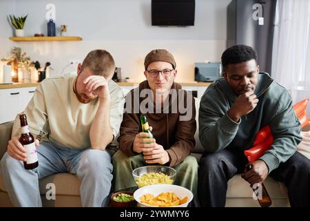 Porträt von drei männlichen Freunden, die zu Hause auf der Couch sitzen und mit gemischten Emotionen fernschauen Stockfoto