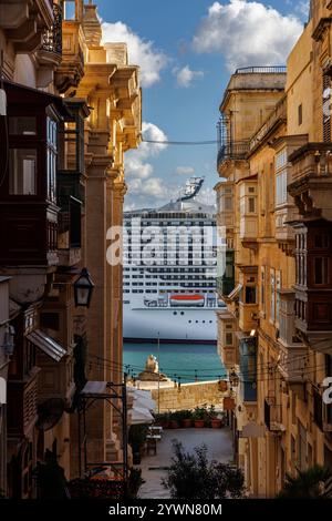 Ein großes, riesiges Kreuzfahrtschiff im Hafen von Malta ist zwischen zwei Häusern in einer alten Valetta Straße zu sehen Stockfoto