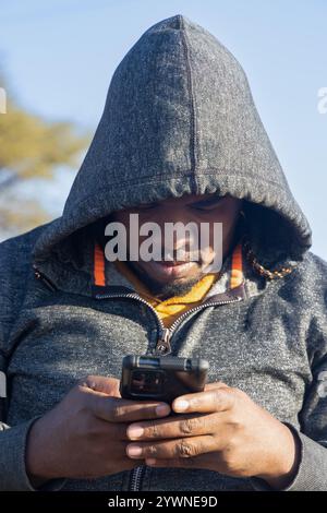 Ich benutze das Smartphone eines jungen afrikanischen Mannes mit einem Hoodie, draußen Stockfoto