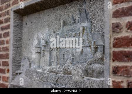 Eine Nahaufnahme eines detaillierten Steinreliefs, das eine historische Burg mit Türmen und steilen Dächern darstellt, die in eine Backsteinmauer eingefasst ist und komplizierte Handwerkskunst zeigt Stockfoto