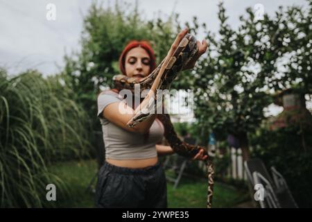 Mädchen, das große Schlange in üppig grünem Garten umgeht Stockfoto