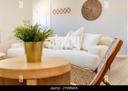 Das helle Wüstenwohnzimmer verfügt über eine weiße Leinencouch mit beigefarbenen Kissen, einen hölzernen Beistelltisch und einen gewebten Stuhl. Stockfoto