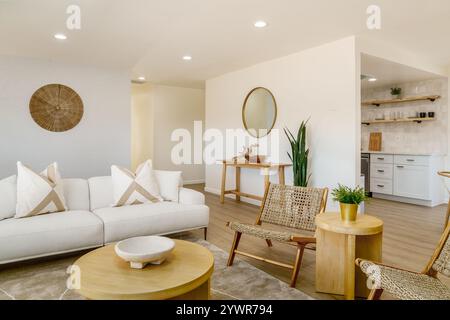 Helles, wüstendes Wohnzimmer mit weißem Sofa, hellen Holzmöbeln, gewebten Stühlen und einer neutralen Farbpalette. Stockfoto