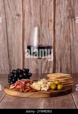Lebensmittelfotografie von Rotwein, Käseparmesan, Schinken, Oliven, Pekannuss, Trauben, Cracker, Vorspeise, Weinglas, Sortiment, Partymahlzeit Stockfoto