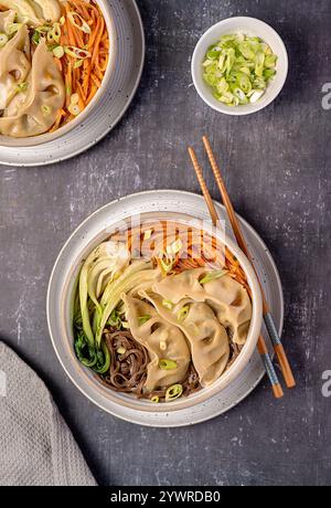 Lebensmittelfotografie von Suppen-Ramen mit Gemüsegyoza-Knödeln, Soba, Buchweizennudeln, Frühlingszwiebeln, Karotten, Bok Choy, Essstäbchen; veganes Essen, Chinesisch Stockfoto
