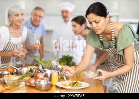 Aufmerksame Frau mittleren Alters, die an einem Kochkurs teilnimmt und eine Mahlzeit aus Lachsfisch dekoriert Stockfoto