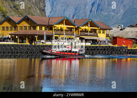 Beliebtes Touristendorf Flam mit lokalen Geschäften und Geschäften zusammen mit einem Fjord-Safari-Boot im Hafen. Stockfoto