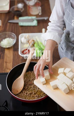 Frau, die Tofu in gebratenes Hackfleisch legt Stockfoto