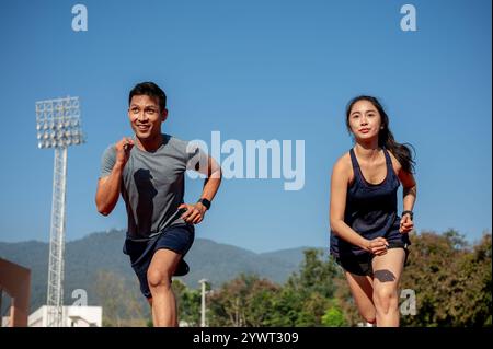Zwei entschlossene asiatische Athleten, die an einem sonnigen Tag auf einer Strecke in einem Stadion laufen. Wettkampf, Herausforderung, Sportspiel, Training Stockfoto