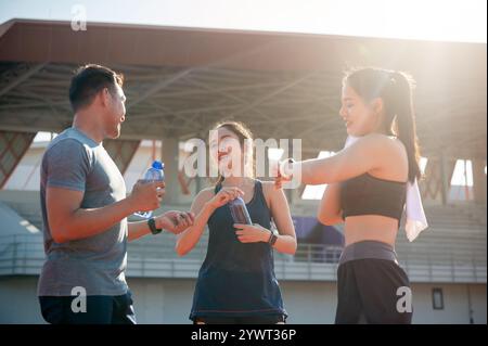 Eine Gruppe asiatischer Läufer genießt nach dem Training in einem Stadion an einem hellen, sonnigen Tag eine Unterhaltung, während sie sich auf einer Laufstrecke ausruhen. Personen und Stockfoto