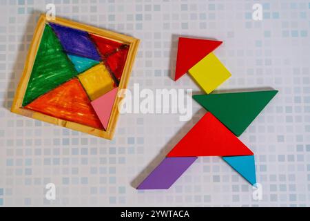 Ein farbenfrohes Tangram-Puzzle, das eine Figur mit seinem Behälter auf einem Holztisch bildet. Stockfoto