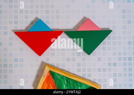 Ein farbenfrohes Tangram-Puzzle, das eine Figur mit seinem Behälter auf einem Holztisch bildet. Stockfoto