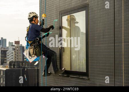 Vom Dach eines Hotels hängender Bauinspektor inspiziert die Fliesen an der Außenseite des Gebäudes in Asakusa Tokio Japan Stockfoto