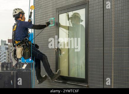 Vom Dach eines Hotels hängender Bauinspektor inspiziert die Fliesen an der Außenseite des Gebäudes in Asakusa Tokio Japan Stockfoto