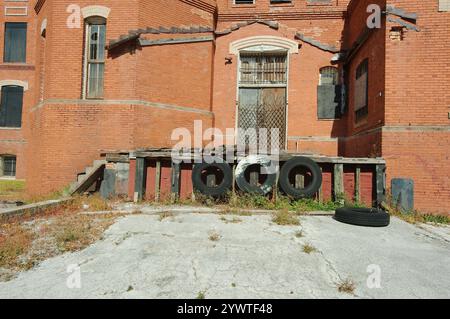 Seite der alten roten Ziegelmauerwerk Ladefläche mit drei schwarzen Reifen am Rand des Docks. Schwarz überdachte Bogenfenster. Sicherheitsbügel aus schwarzem Stahl. Stockfoto