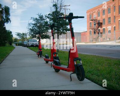 Nur für redaktionelle Verwendung, Tampa, Florida USA, 10. Dezember 2024, führende Linien Red and Black Spin E-Bike auf dem Bürgersteig mit einem alten roten Backsteingebäude auf der rechten Seite Stockfoto