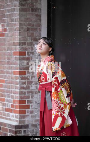 Eine Japanerin im Alter von 20 Jahren, die einen roten Kimono (Hakama) trägt, ein Grundnahrungsmittel japanischer Universitätsabsolventen, steht vor der eisernen Tür einer Kultur Stockfoto