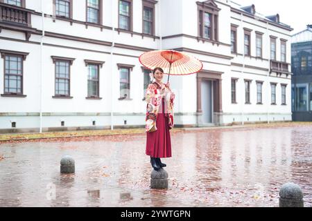 Eine Japanerin im Alter von 20 Jahren, die einen roten Kimono (Hakama) trägt, ein Grundnahrungsmittel für japanische Universitätsabsolventen, steht mit einem roten japanischen Regenschirm in der Hand Stockfoto