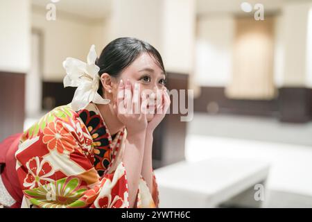 Eine Japanerin im Alter von 20 Jahren trägt einen roten Kimono (Hakama), ein Grundnahrungsmittel für japanische Universitätsabsolventen, während sie mit gefalteten Händen vorne sitzt Stockfoto